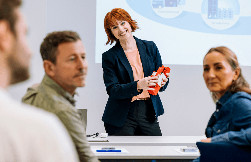 Referentin in einem VdS-Seminar erläutert anhand eines Anschauungsobjekts die Sicherheit elektrischer Anlagen, im Hintergrund eine Präsentation mit Anlagenschemata - steht für praxisnahe Fortbildung zu Planung, Prüfung und Instandhaltung elektrischer Anlagen.